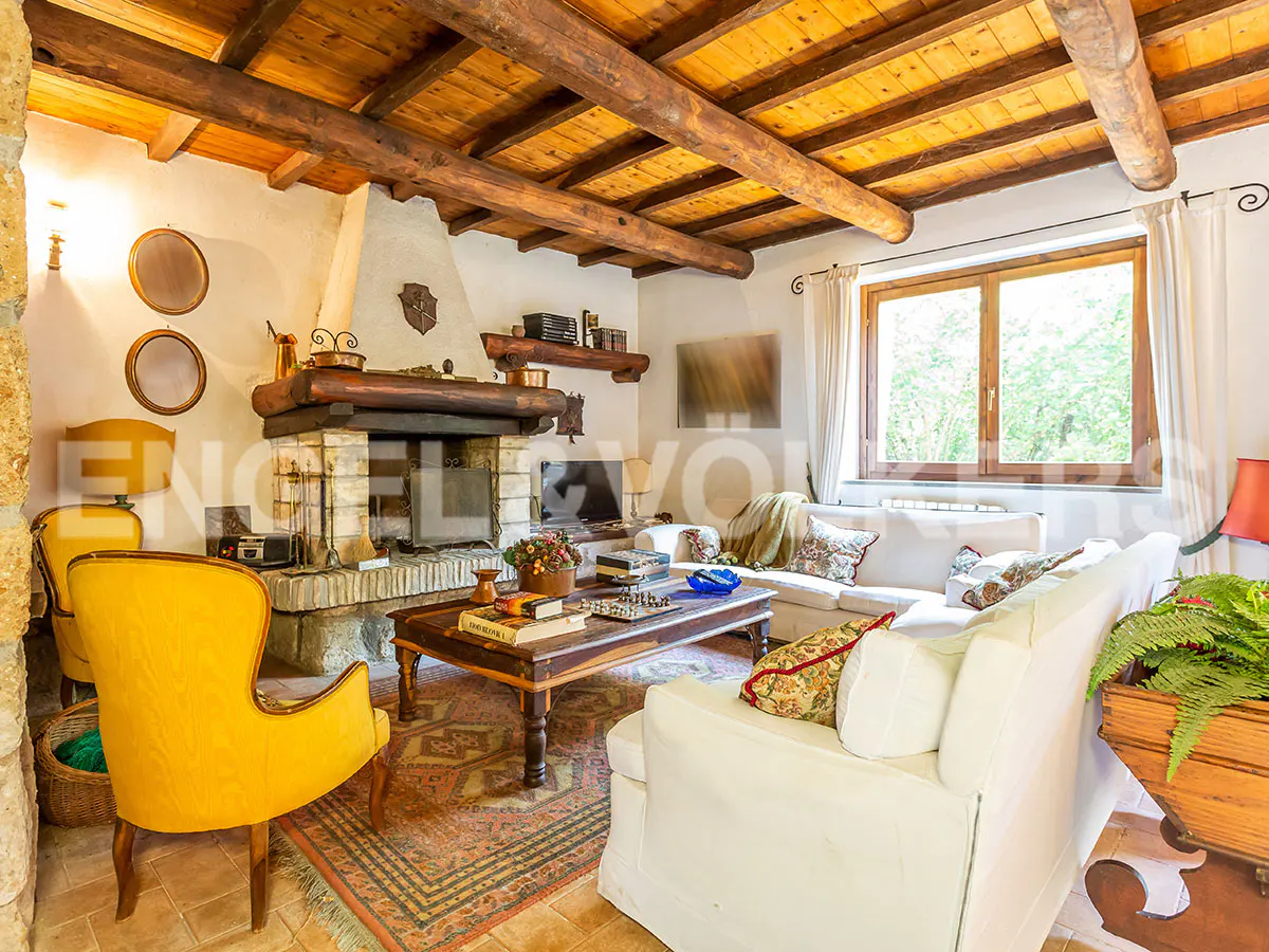 Living room with exposed wood beam ceiling, stone fireplace, yellow chair, white sofa, and large wood coffee table.