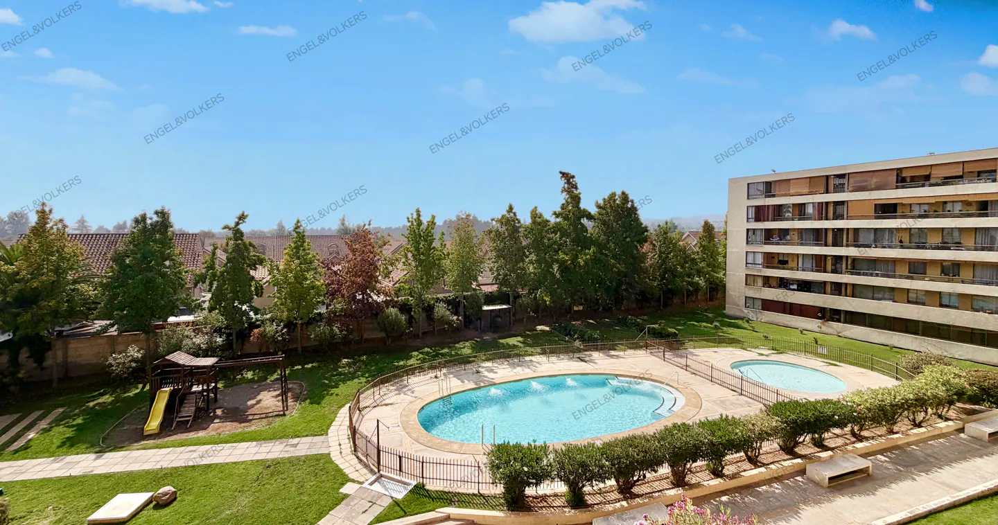 Aerial view of a building with a pool, playground, and green space on a sunny day.