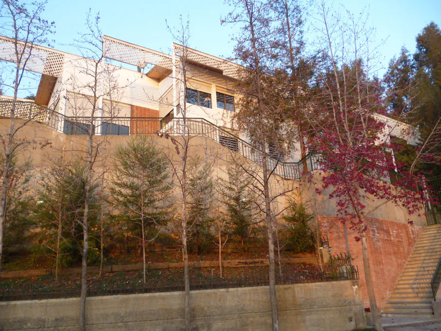 Exterior view of a modern white building on a hill, with trees and stairs leading up to it.