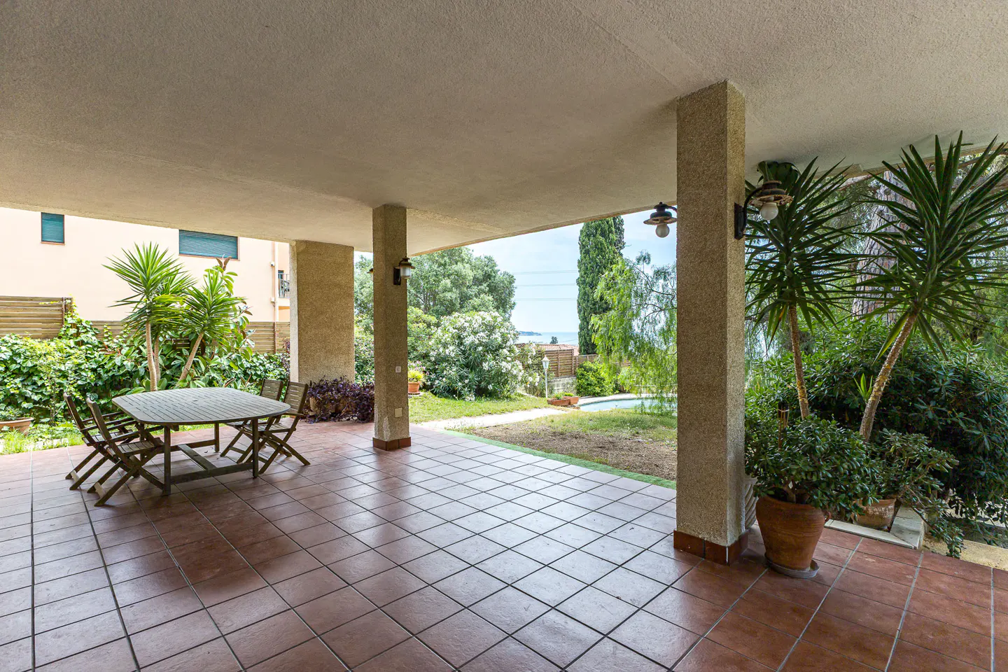 Covered patio with tile floor, table, chairs, and view of green lawn, trees, and ocean in the background.