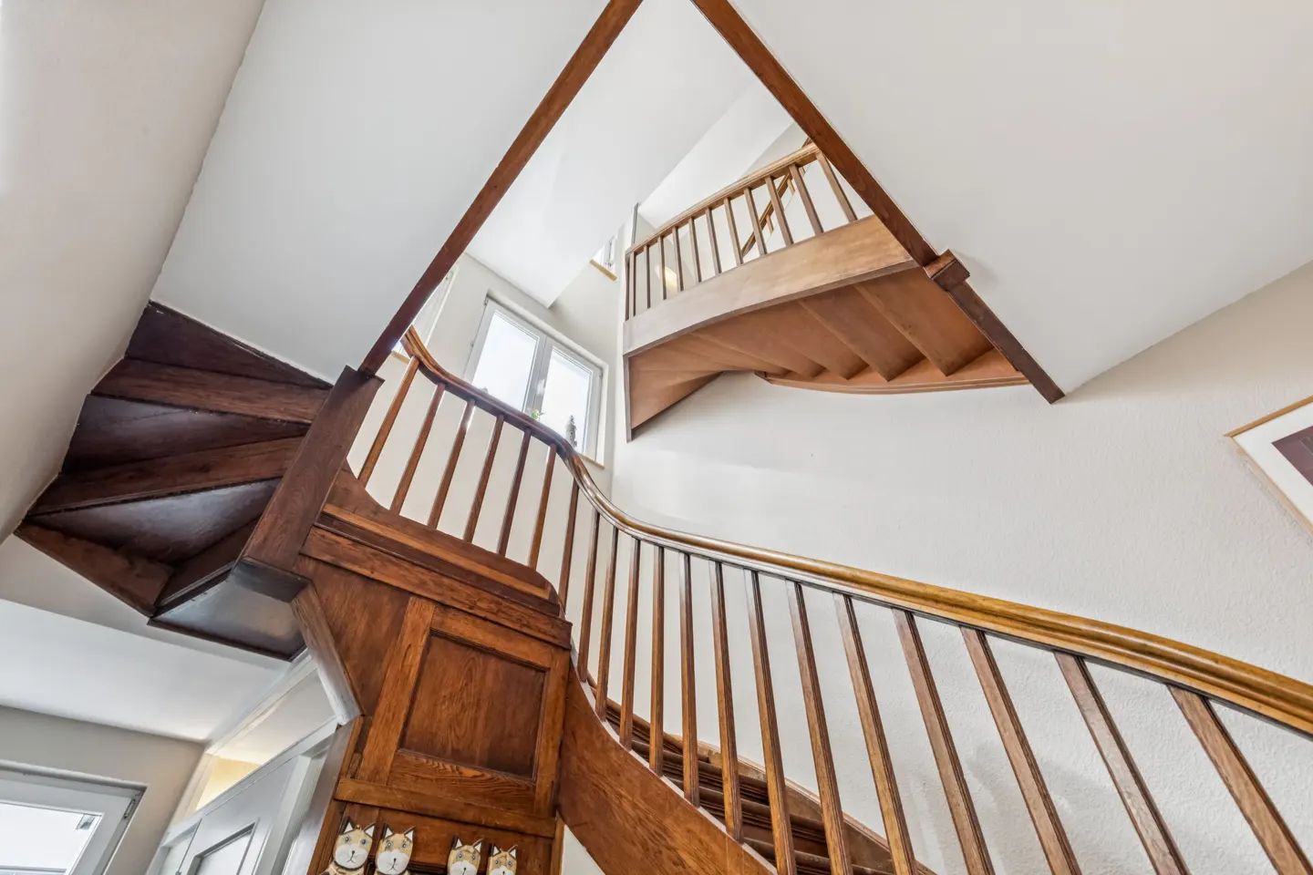 A low-angle shot of a wooden staircase with white walls and a window in the background.