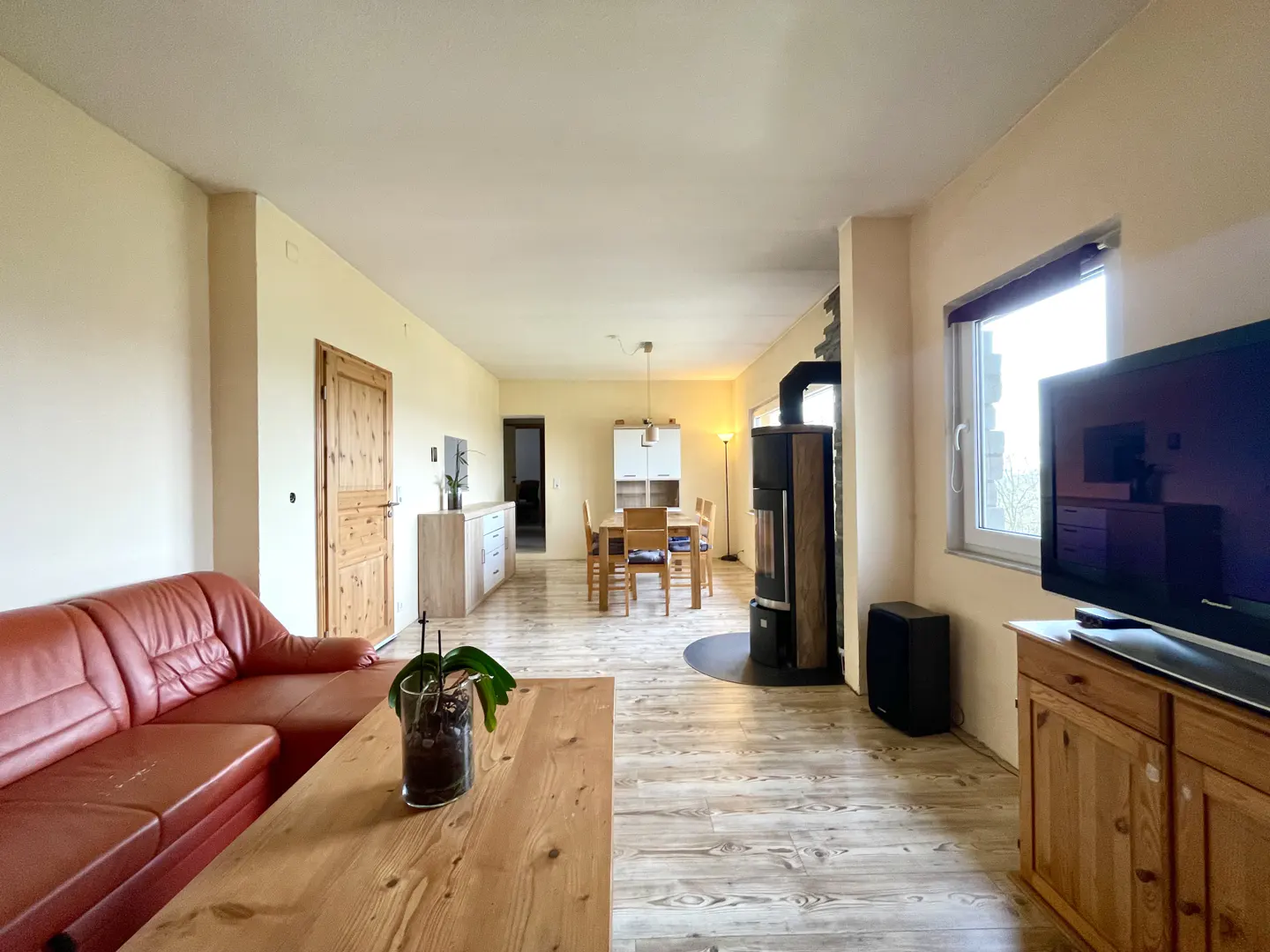 A living room with a red leather sofa, wood table, wood-burning stove, and dining table with chairs.