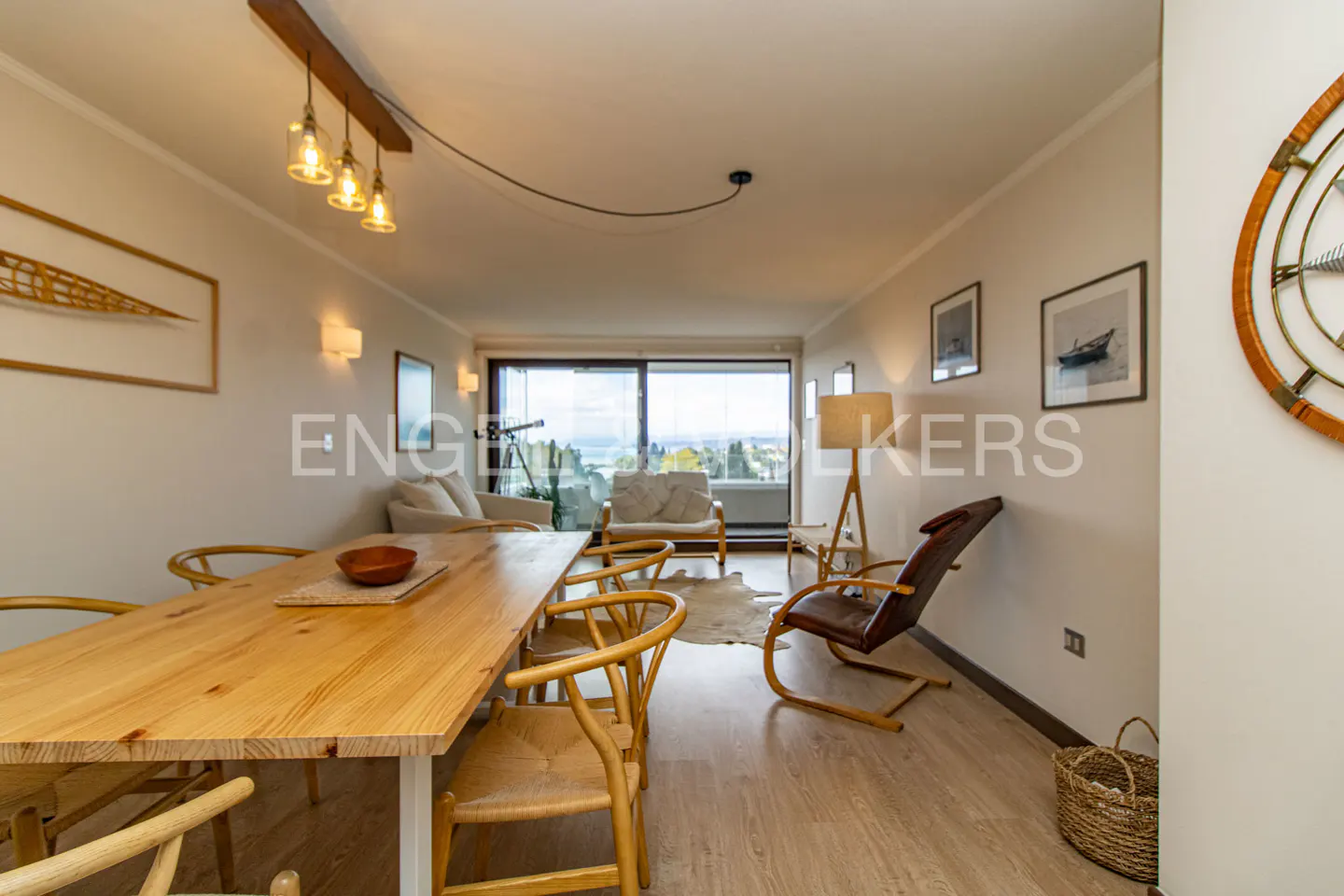 Bright living room with a wooden table, chairs, and a view of the water through a large window.