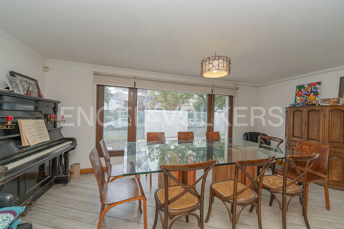 Dining room with a glass table, six wooden chairs with cane seats, a black upright piano, and a large wooden cabinet.