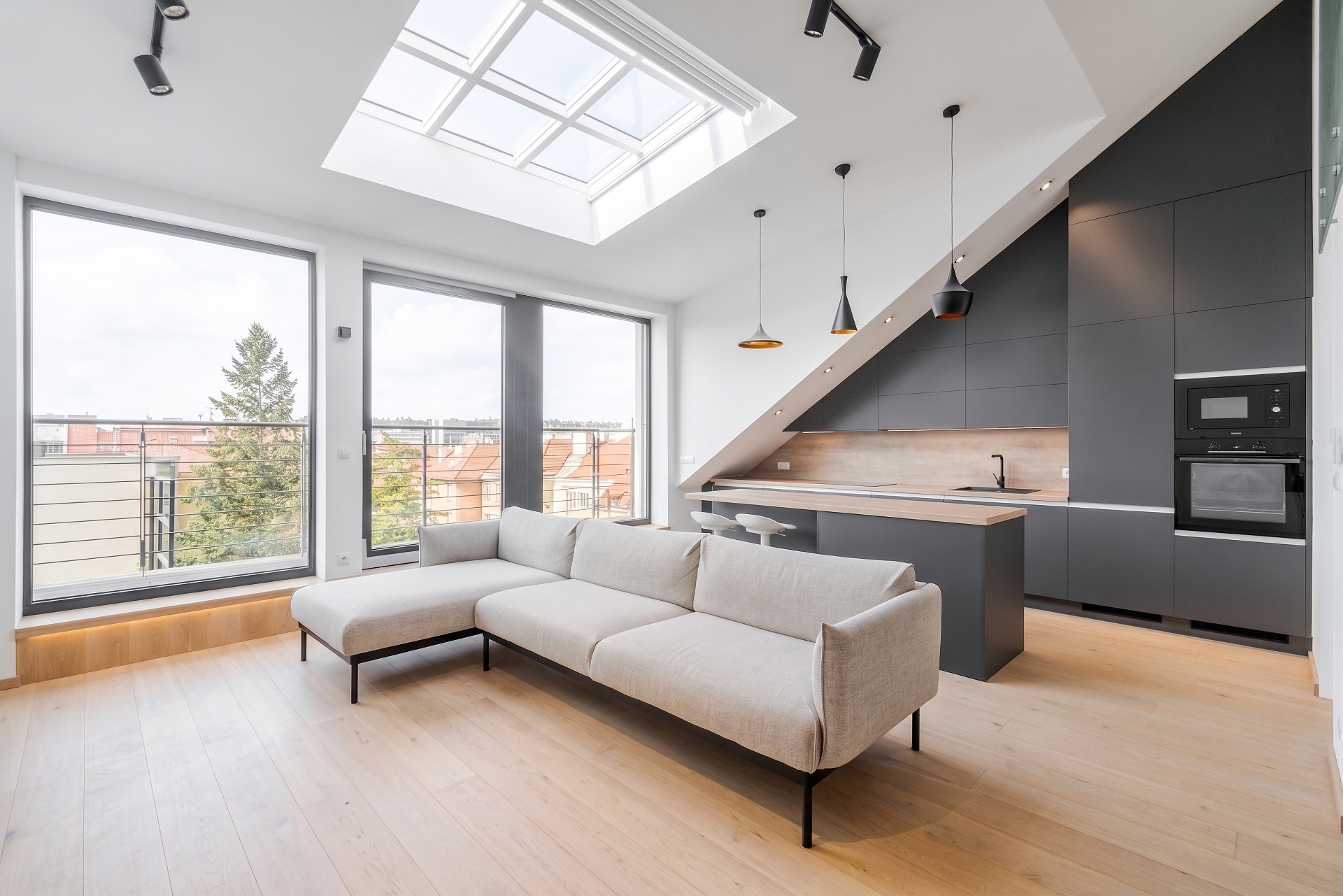 Modern open-plan living room with a white sectional sofa, skylight, and a sleek dark grey kitchen with light wood floors. [AI-generated text]