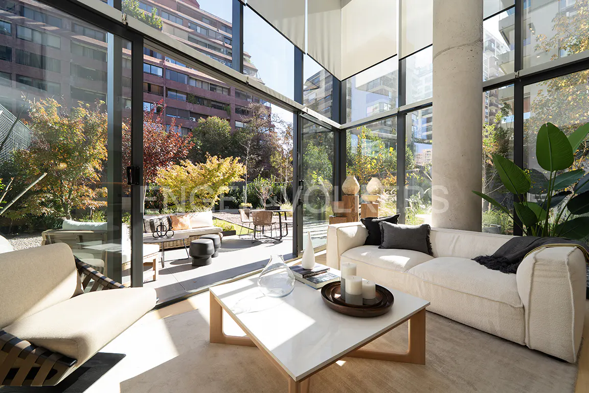 Bright living room with a white sofa, marble coffee table, and floor-to-ceiling windows overlooking a lush garden.