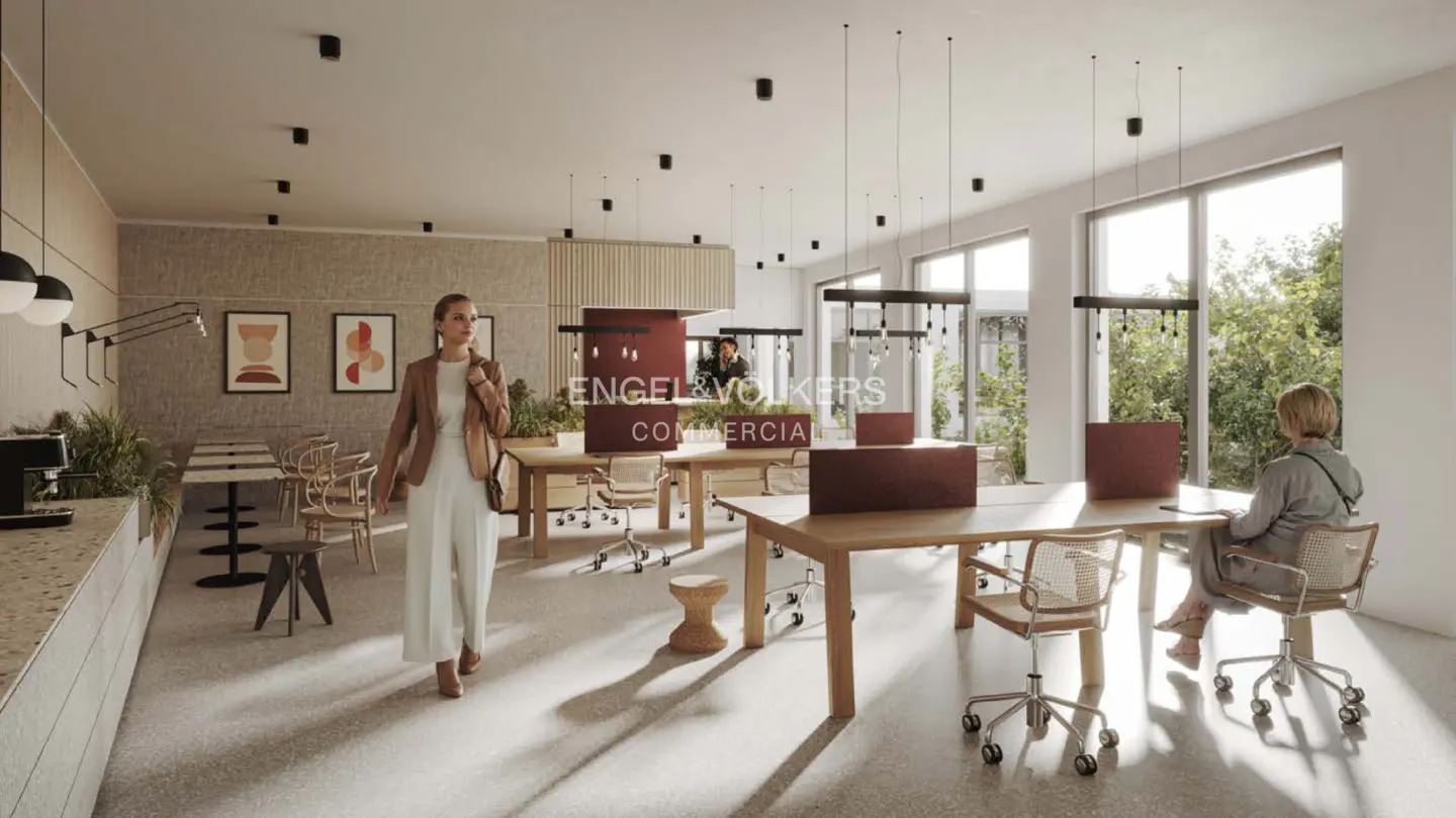 Bright office space with wooden desks, chairs, and pendant lights. A woman in a blazer walks by the Engel & Volkers Commercial sign.