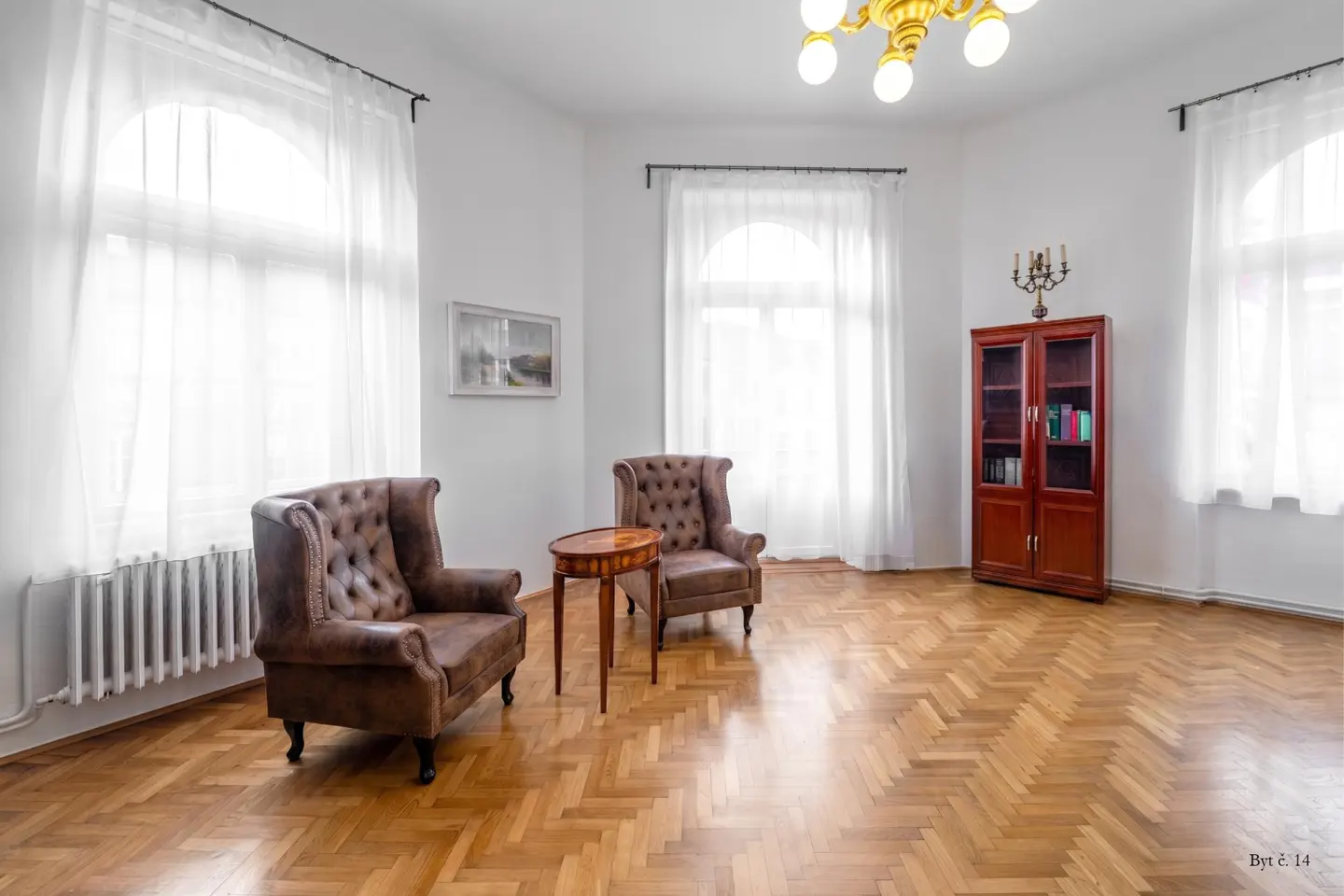 Bright room with herringbone wood floors, two brown leather armchairs, a small side table, and a tall wooden cabinet.