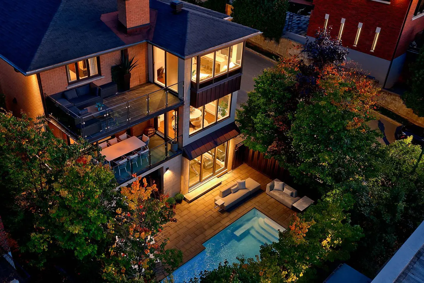 Aerial view of a modern brick house with a pool, patio furniture, and balconies at dusk.