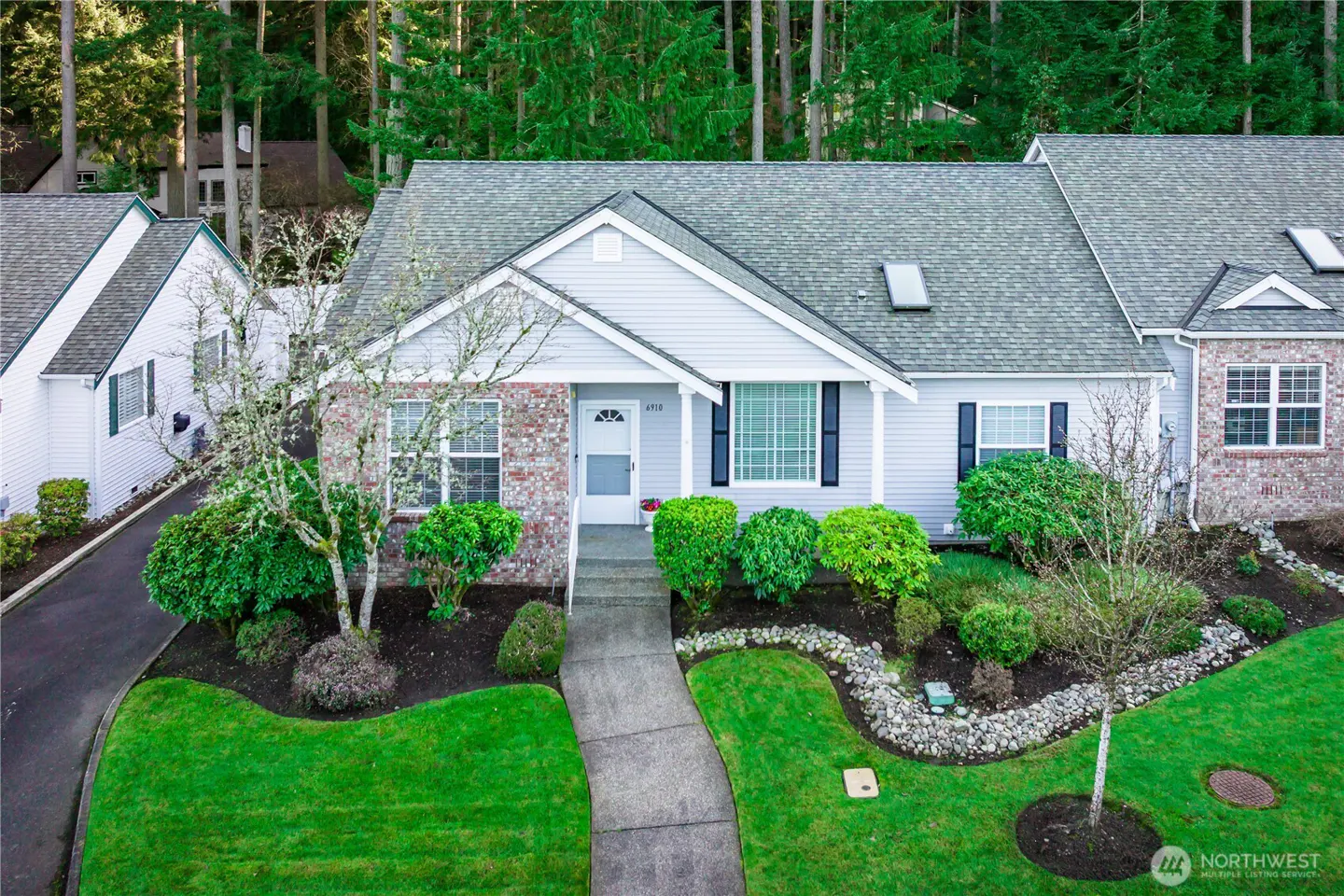 Aerial view of a light blue single-story house with brick accents, a gray roof, and a well-manicured green lawn.