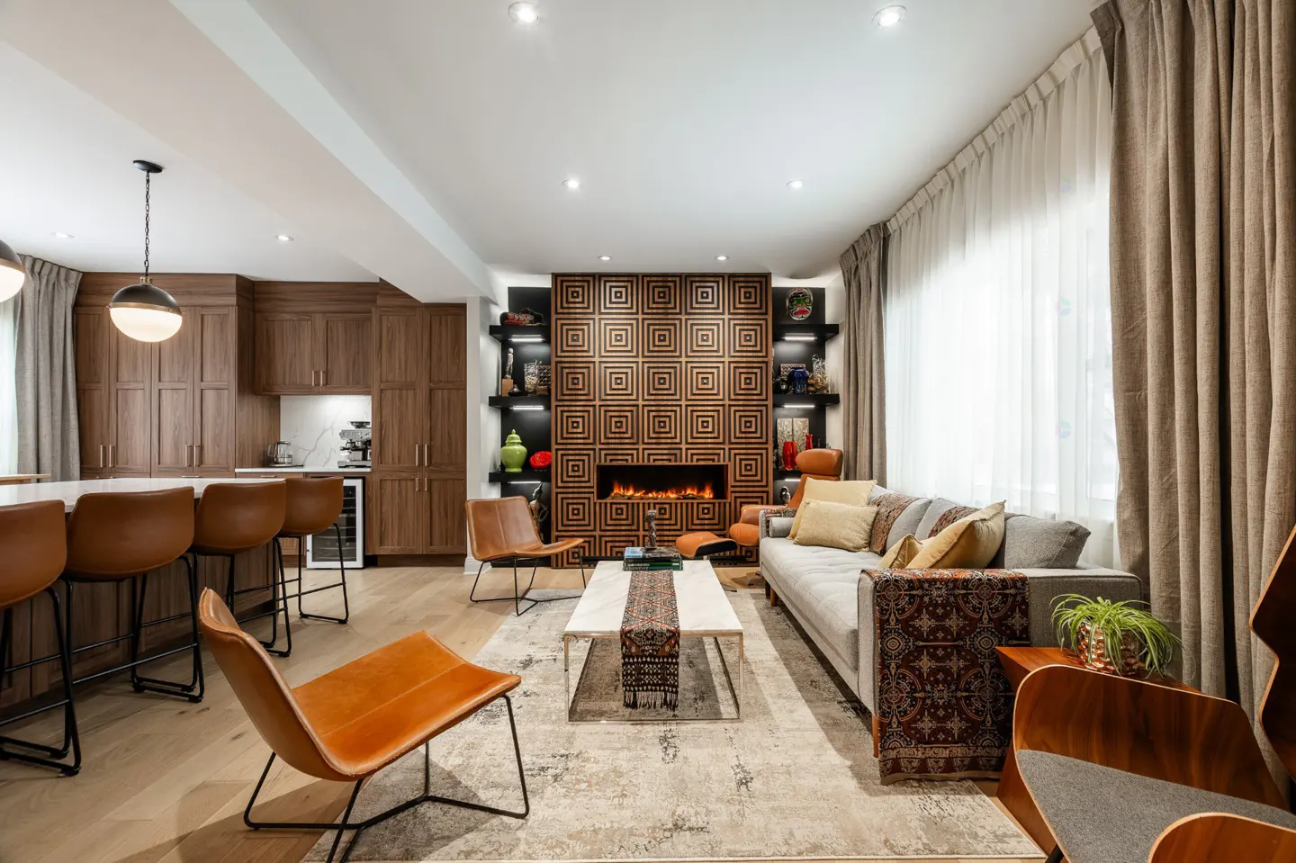 Open-concept living space with a kitchen, fireplace, and seating area. Brown cabinets, leather chairs, and a gray sofa furnish the room.