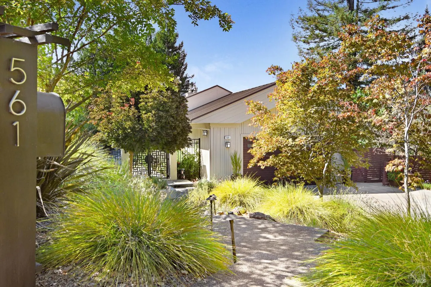 Exterior of a modern home with a stone walkway, lush landscaping, and a mailbox with the number 561.