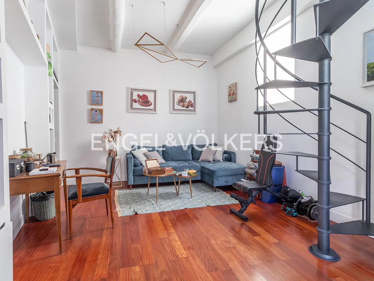 Living room with hardwood floors, a blue sectional sofa, a desk, and a black spiral staircase.