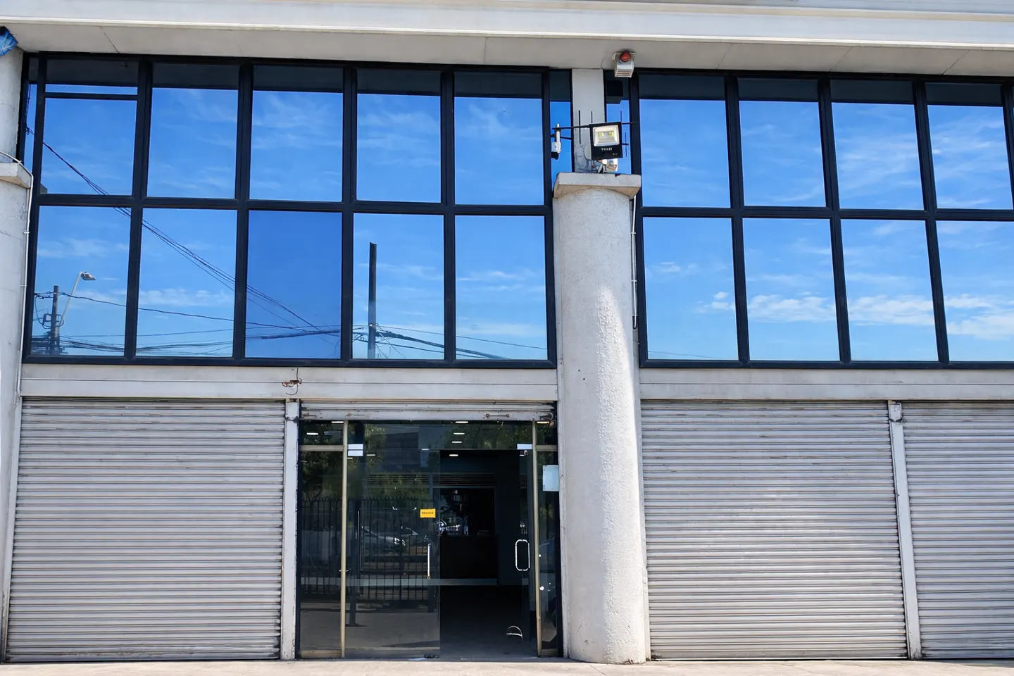 Exterior of a commercial building with blue-tinted windows, gray roll-up doors, and a glass entrance.