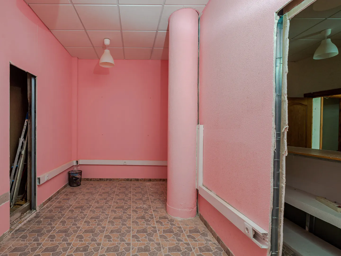 A pink room with a tiled floor, a column, and an open doorway with a ladder inside.