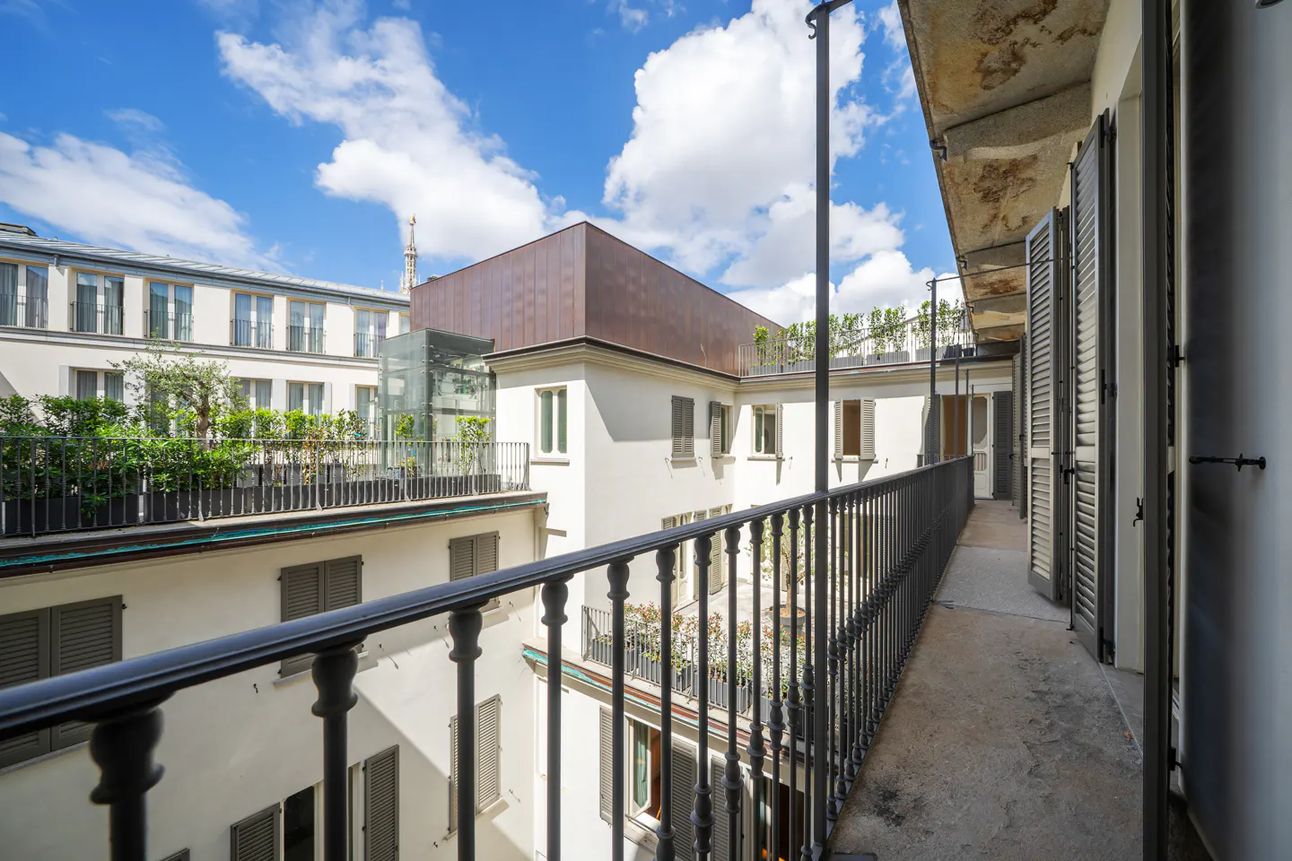 Balcony view of a white building with gray shutters and a black railing, under a blue sky with white clouds.
