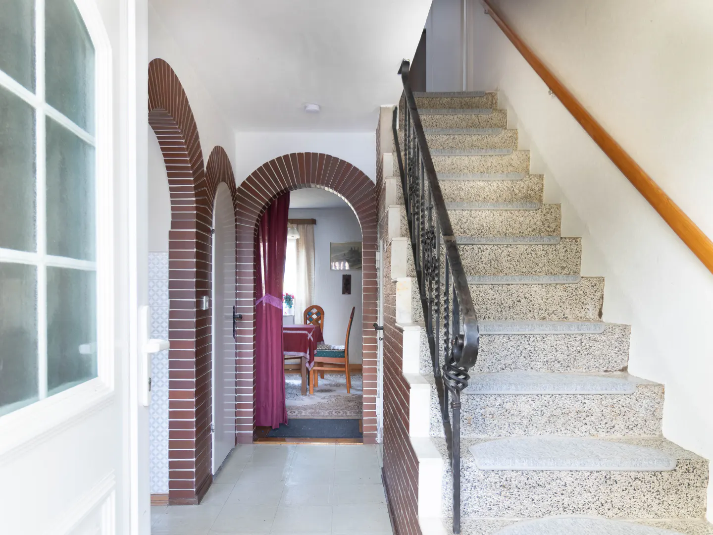 Entryway with brick arches leading to a dining room, and a staircase with a black metal railing.