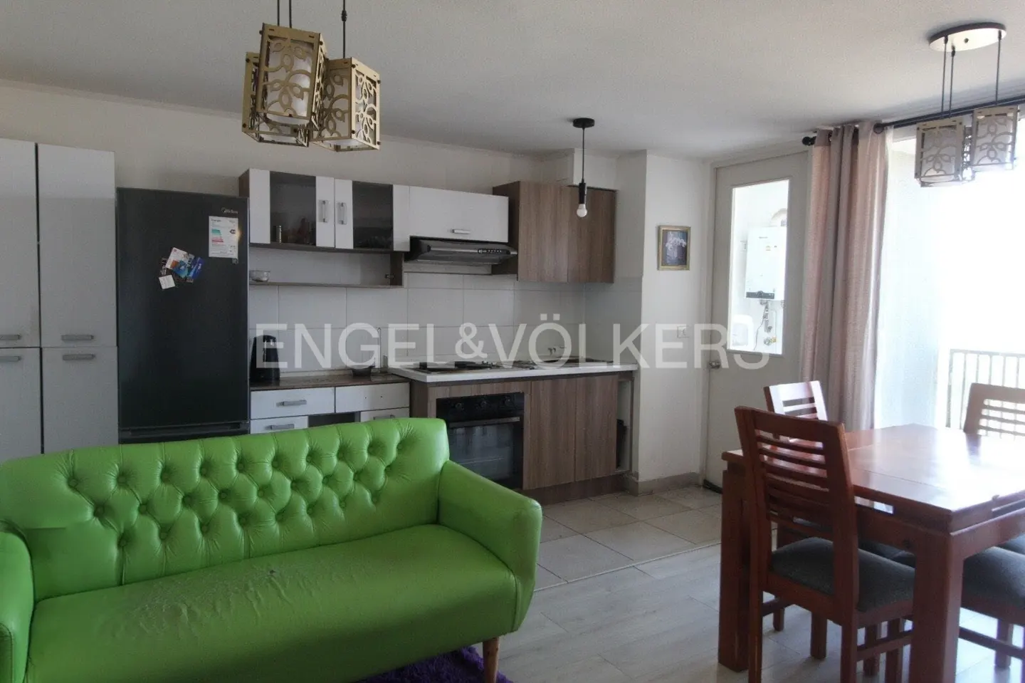 Open-concept kitchen and dining area with a green sofa, wooden table and chairs, and modern appliances.