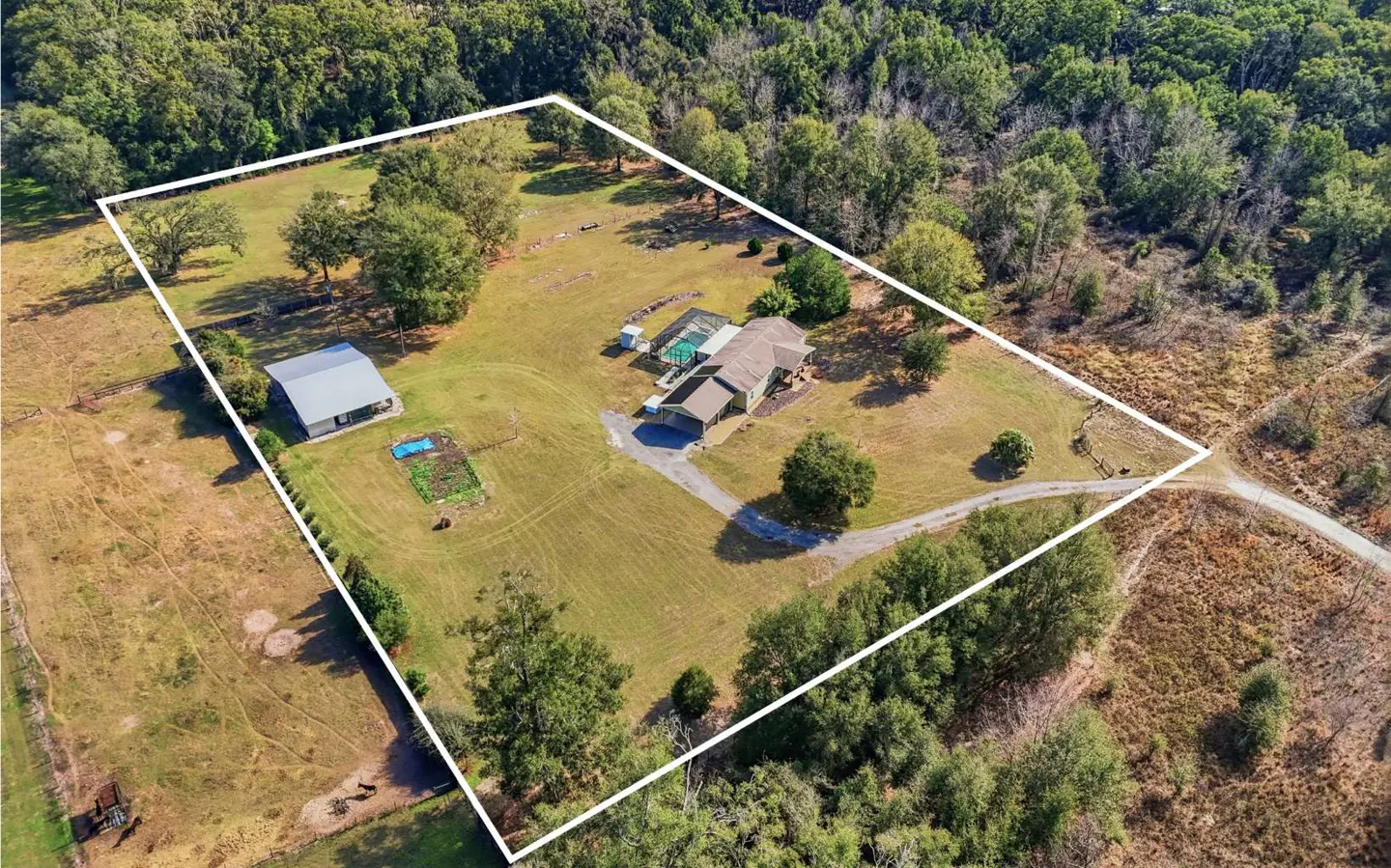 Aerial view of a property with a house, pool, barn, and garden, surrounded by trees and outlined in white.