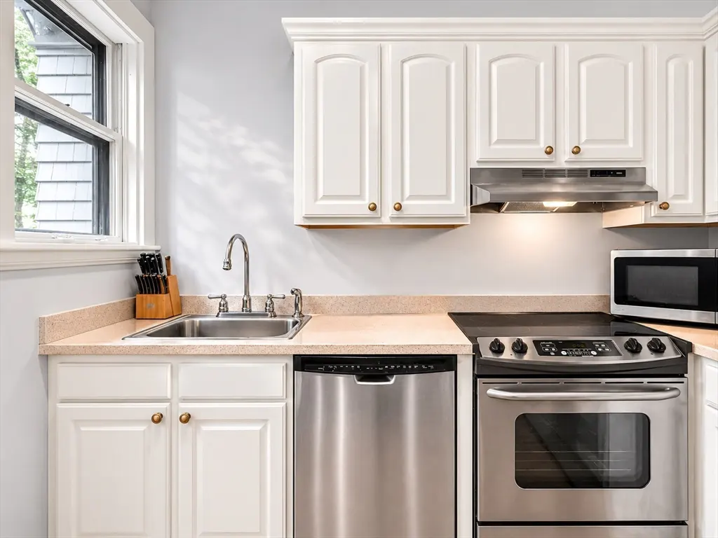A bright kitchen with white cabinets, stainless steel appliances, and a window.