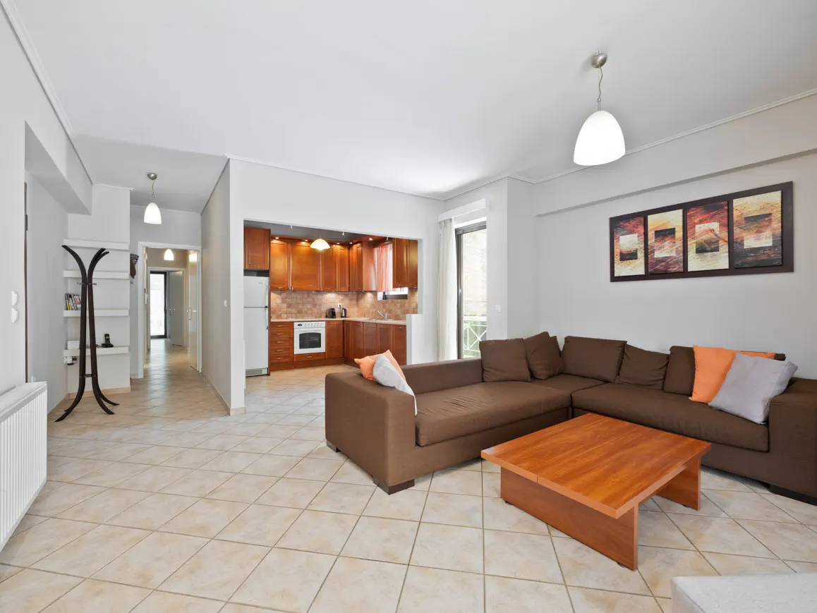 Open-concept living space with brown sectional sofa, wood coffee table, and kitchen with wood cabinets.