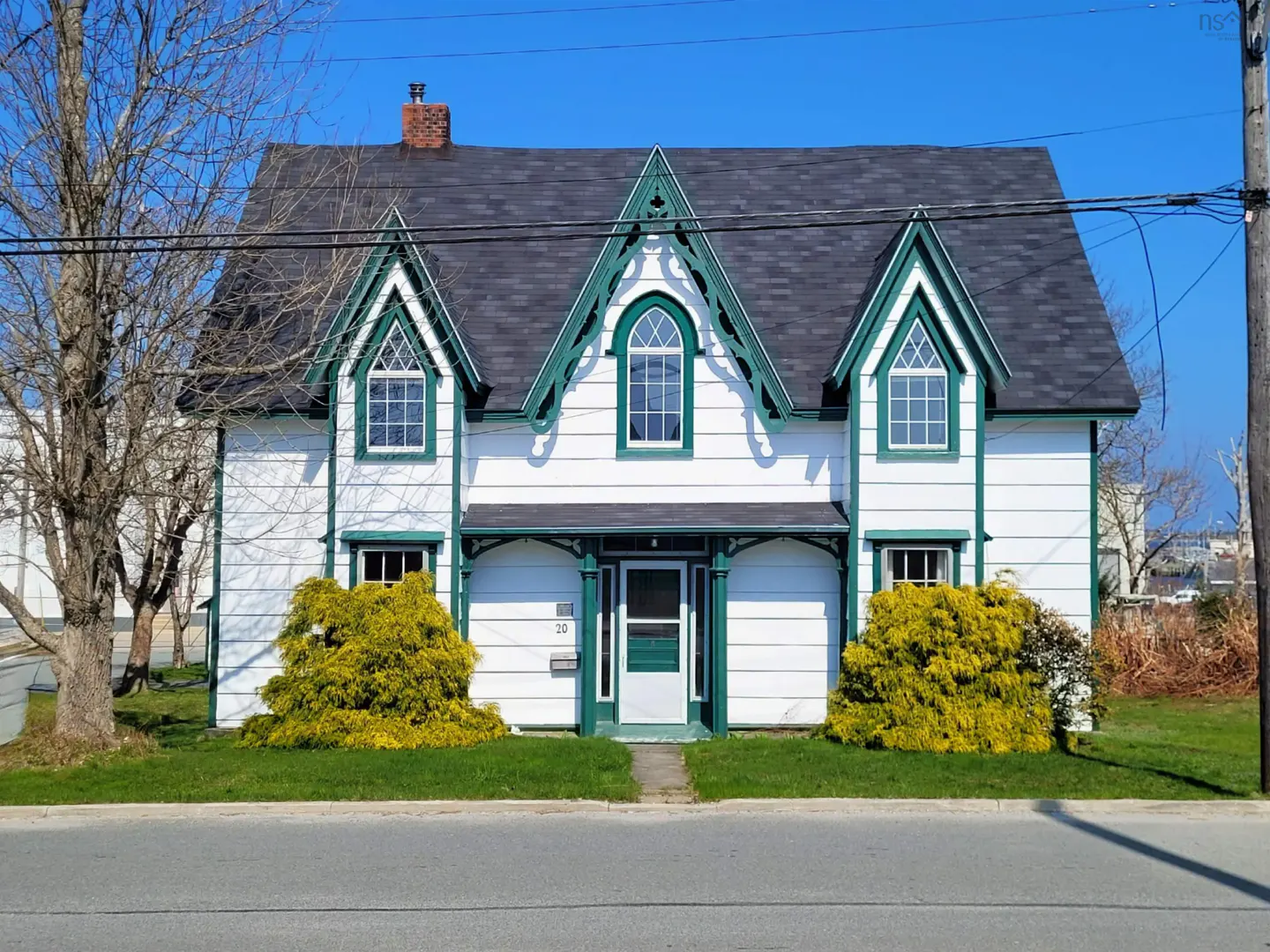 Two-story white house with green trim and a dark roof on a sunny day.