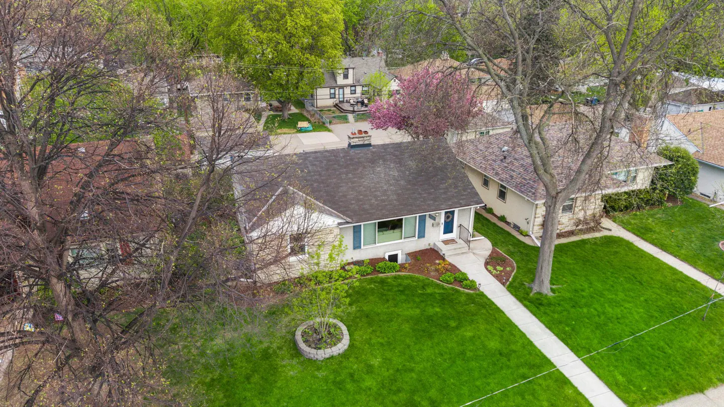 Aerial view of a single-story house with a gray roof, blue door, green lawn, and a sidewalk leading to the entrance.