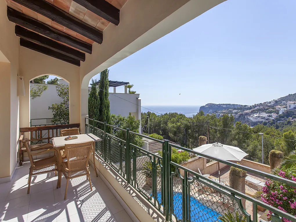 Balcony view of a Mediterranean villa with a table, chairs, pool, and ocean view.
