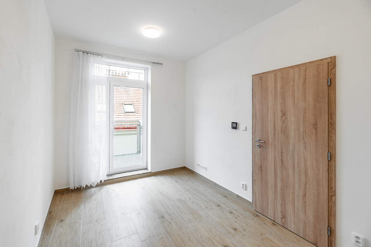 Empty room with white walls, light wood-look flooring, a wooden door, and a glass door leading to a small balcony. [AI-generated text]