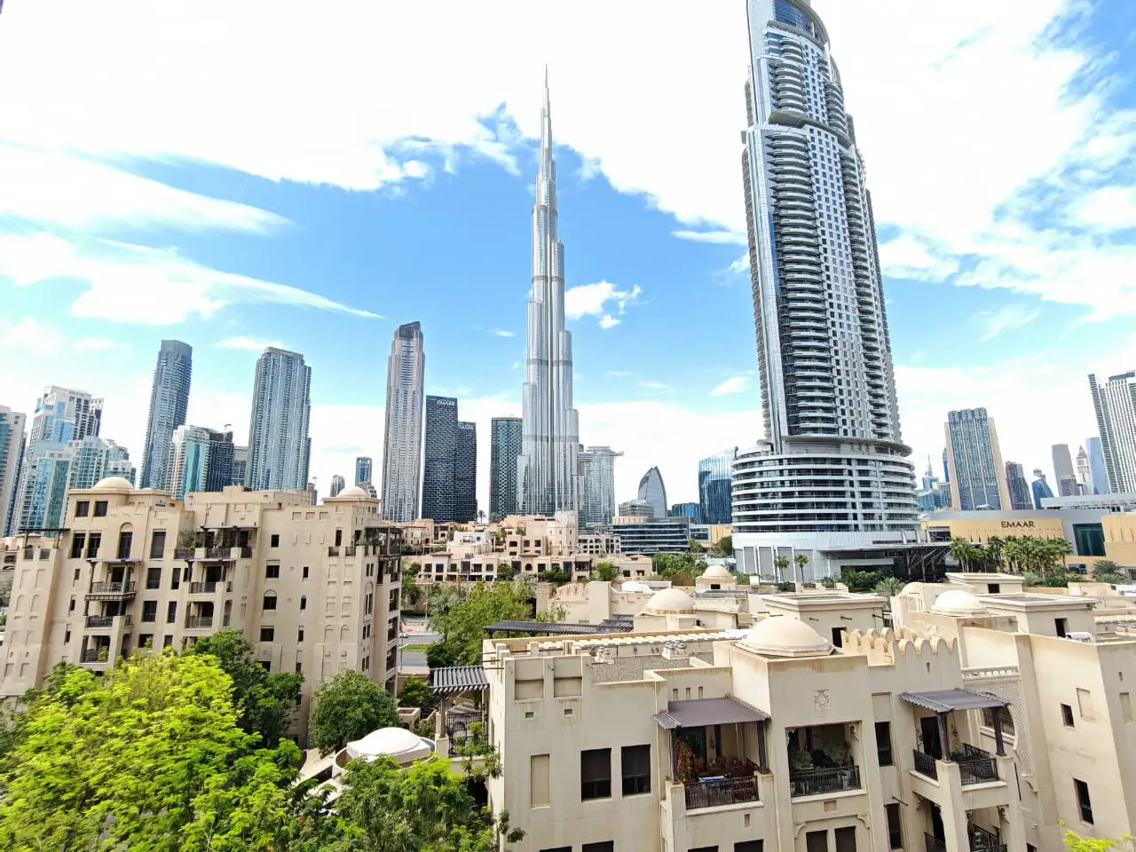 Dubai skyline view featuring Burj Khalifa and modern buildings against a blue sky, with traditional architecture in the foreground.