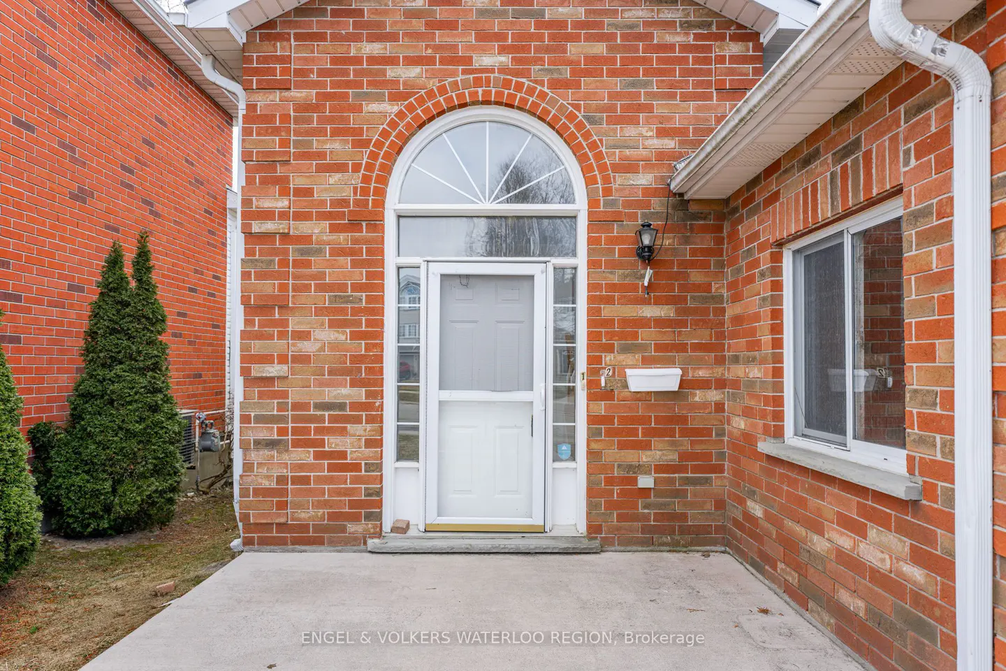 Brick house exterior with a white front door under an arched window. A small white planter hangs on the brick wall.