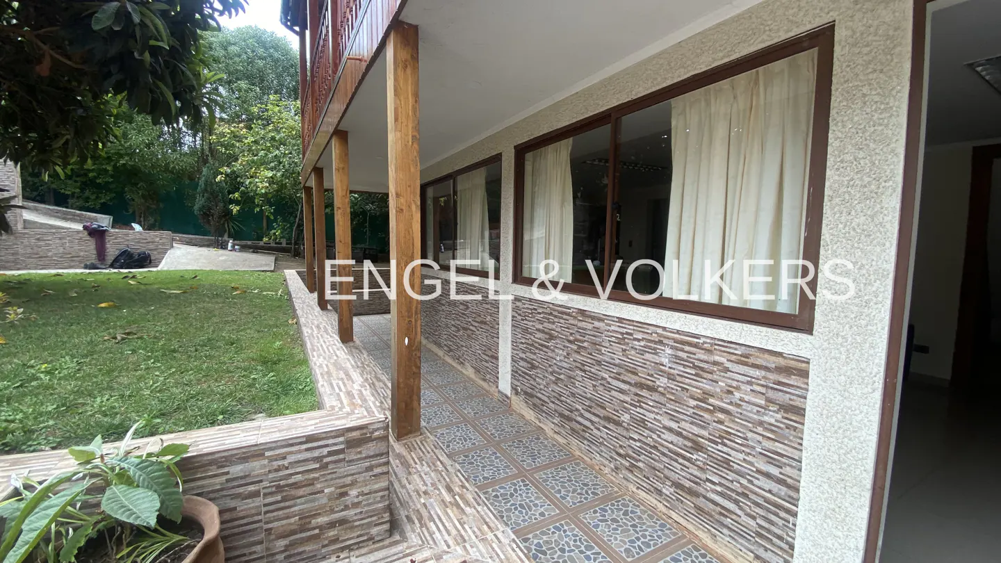 Exterior view of a house with a covered patio, brown window frames, and a green lawn.