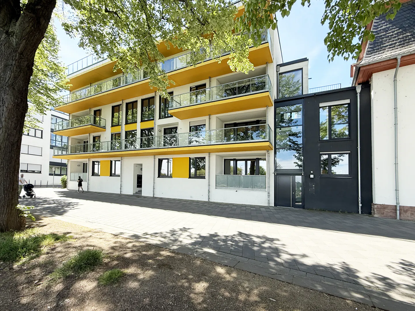 Modern apartment building with yellow accents and glass balconies, next to a black building with reflective windows.