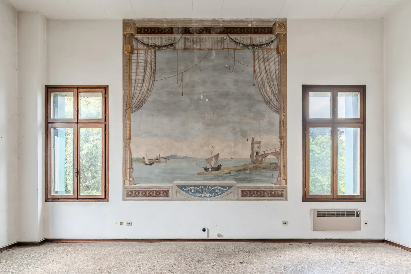 Empty white room with two windows and a large mural of a seascape with boats and a bridge.