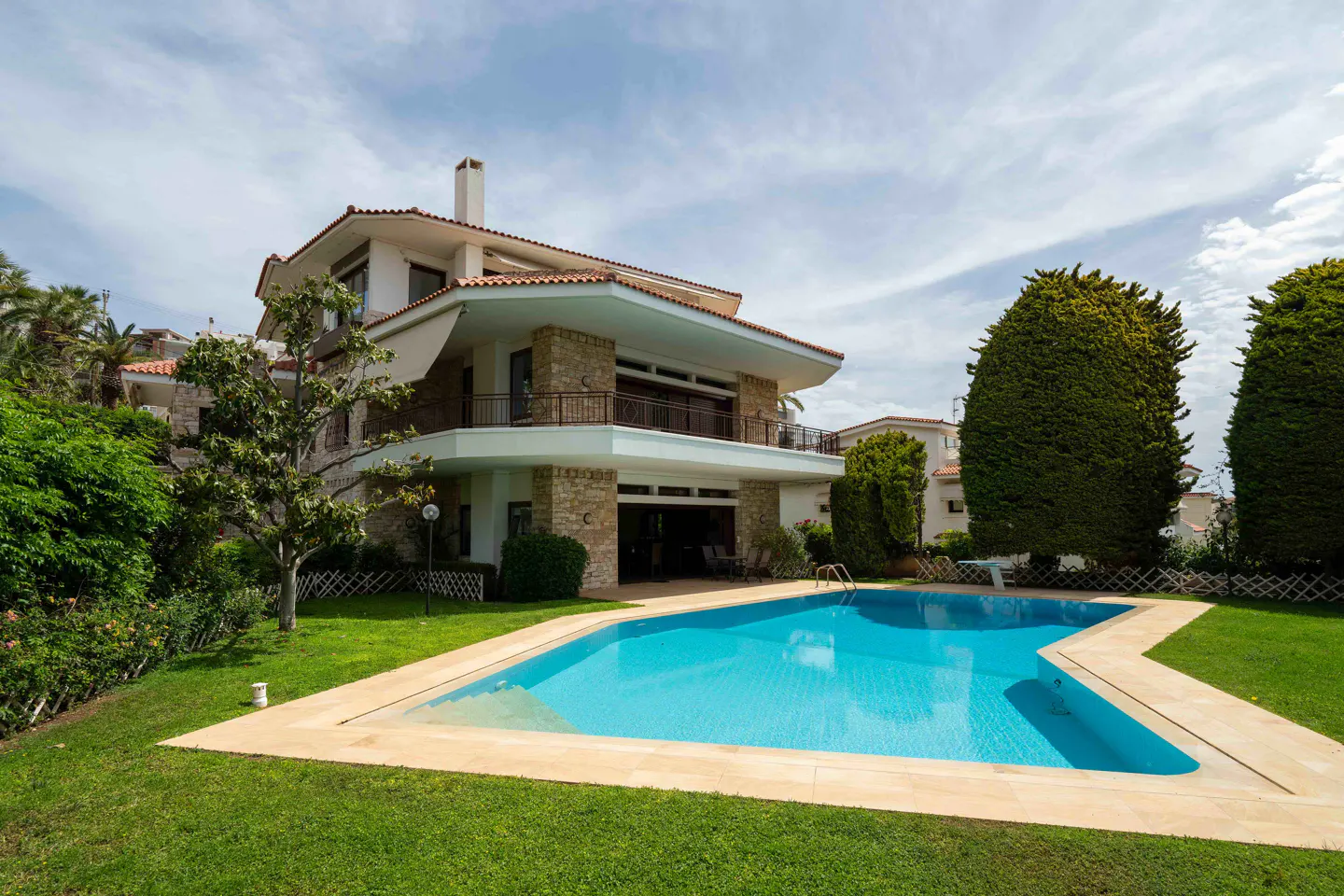 Exterior view of a two-story house with a red tile roof and a blue swimming pool in the backyard.