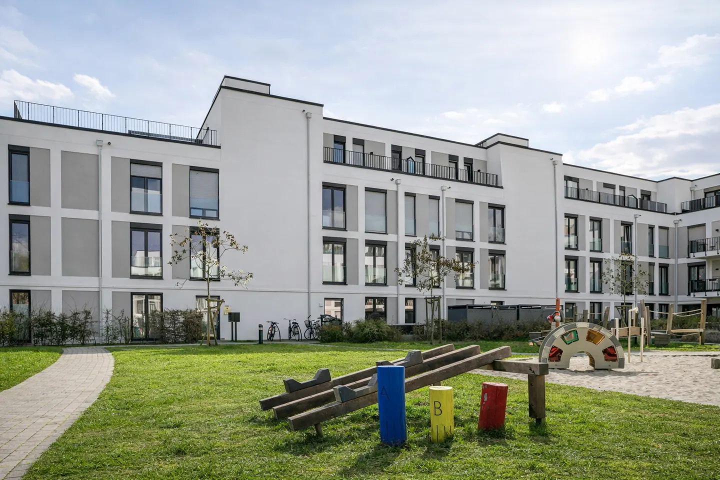Modern white apartment building with a playground on the green lawn in front.