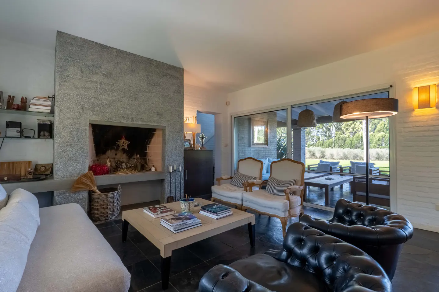 Living room with stone fireplace, white sofa, black leather chairs, and a view of an outdoor patio through sliding glass doors.