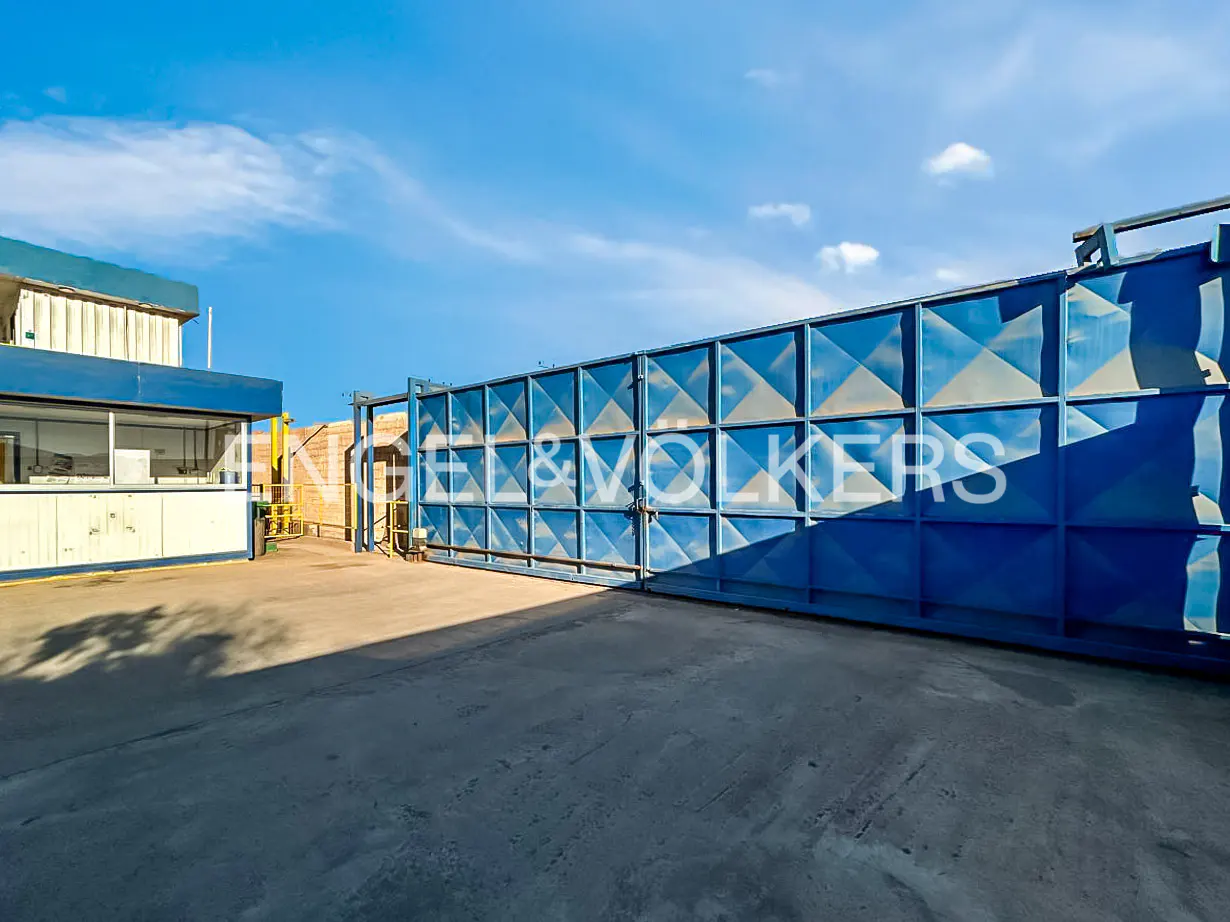 Large blue industrial sliding gate in a paved yard next to a white and blue office building under a clear blue sky.