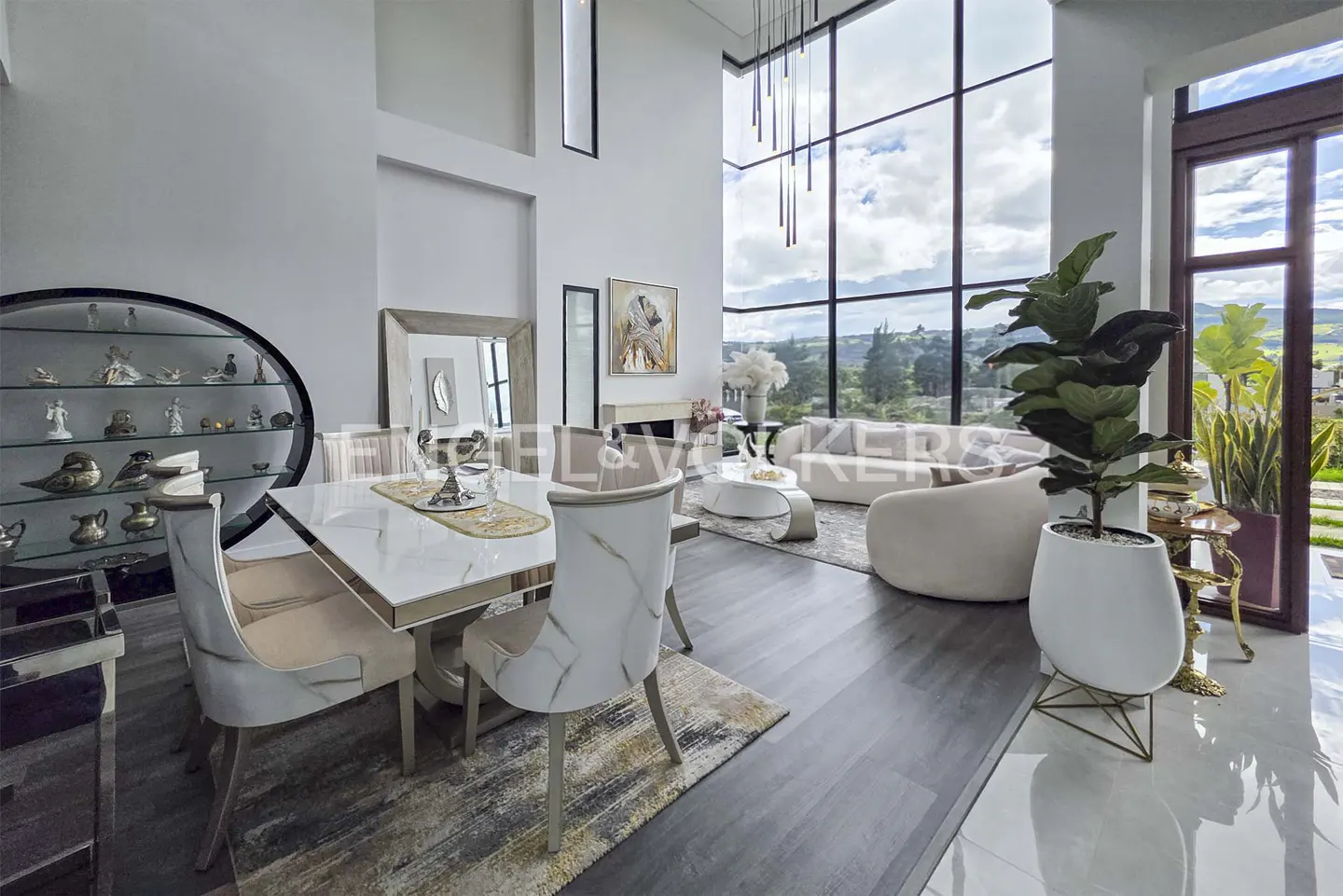 Bright, modern living space with a dining table, white chairs, and a large window with a view of the landscape.