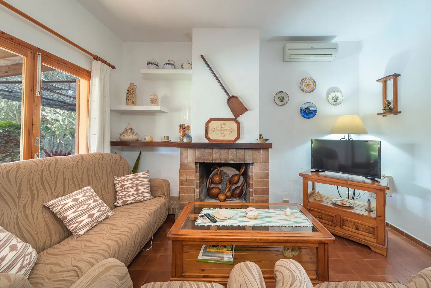 Living room with a brown sofa, brick fireplace, wooden coffee table, and TV. Plates decorate the white wall.