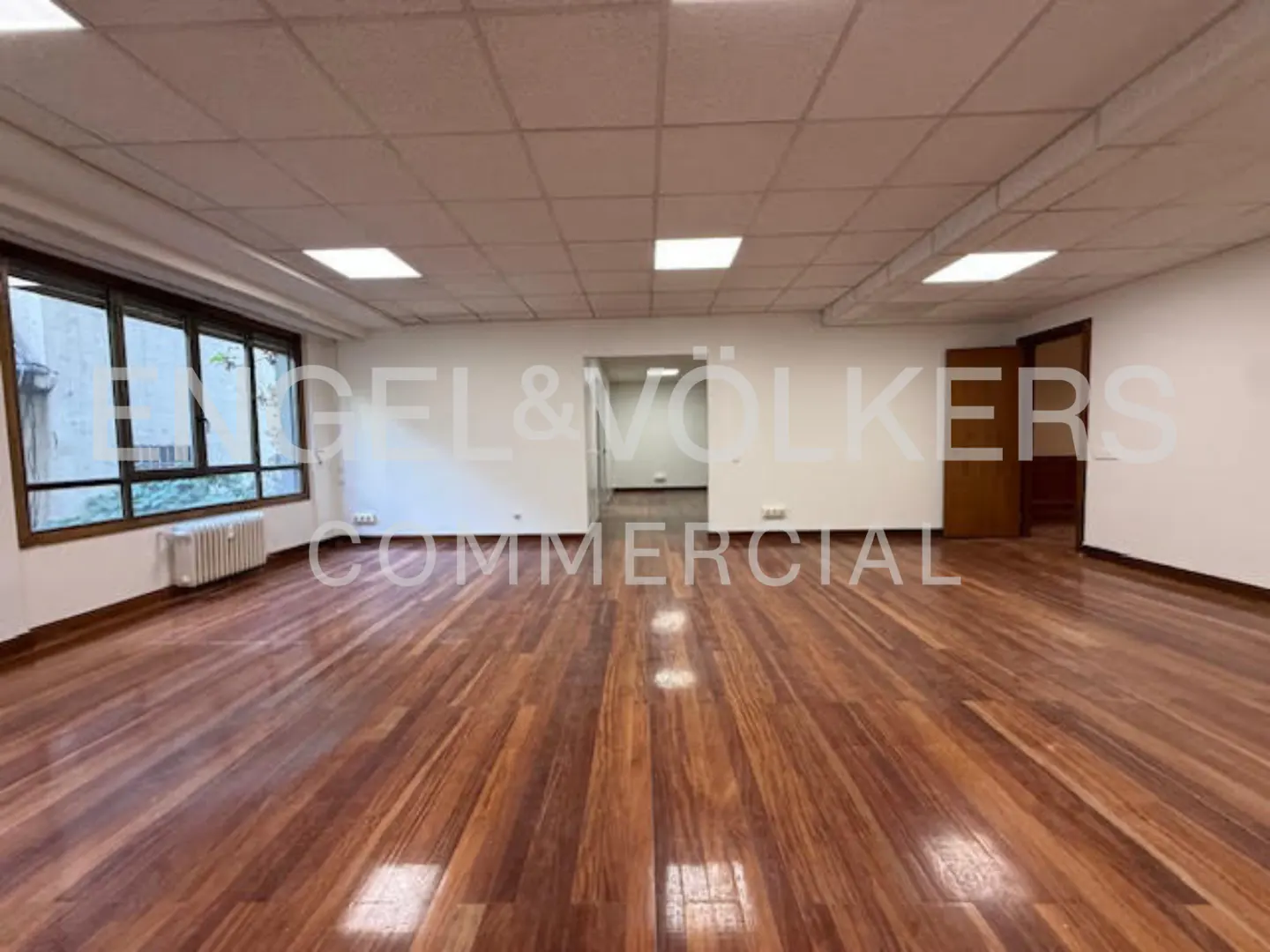 An empty commercial space with hardwood floors, white walls, and a large window.