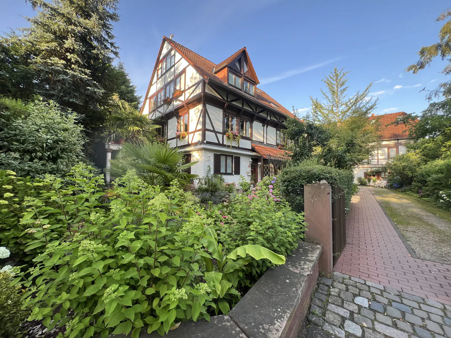 Exterior of a half-timbered house with a red tile roof and lush green landscaping. Brick walkway leads to the house.