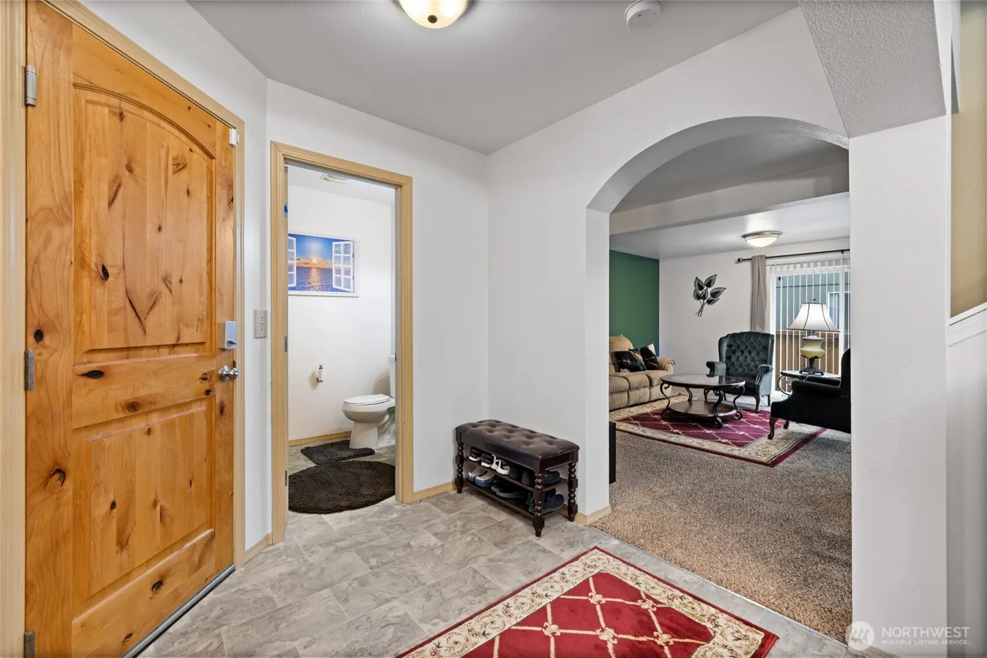 A home's entryway with a wooden door, a bathroom, and a living room visible through an archway.
