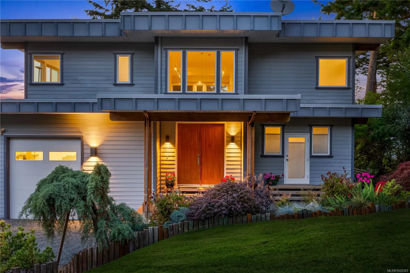 Two-story gray house with a double wooden front door, a garage, and a green lawn.