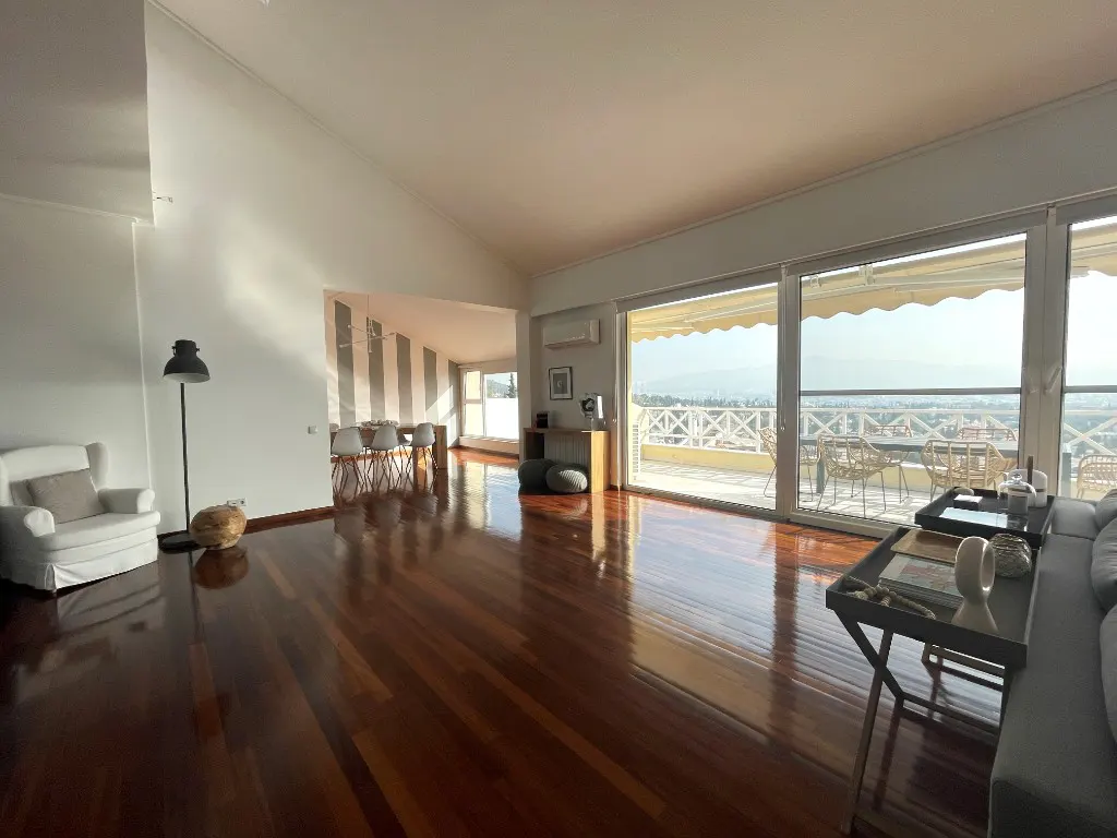 Bright, open living room with hardwood floors, white walls, and large windows leading to a balcony with city views.