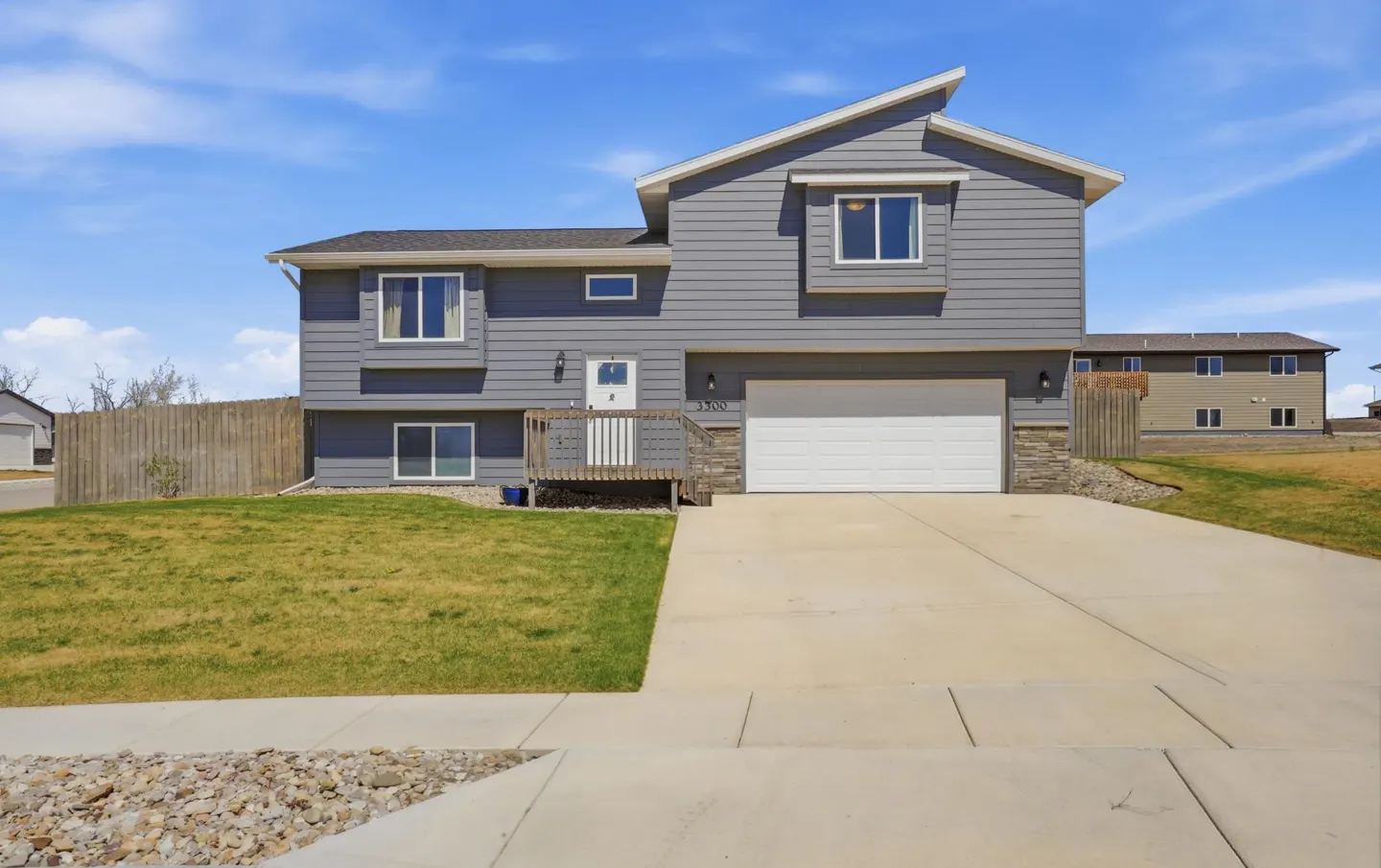 Two-story gray house with white trim, a white garage door, and a concrete driveway under a blue sky.