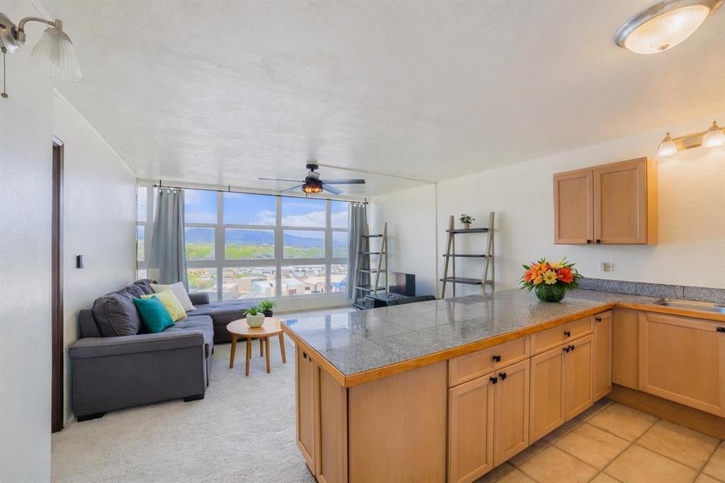 Open-concept living area with a grey sectional sofa, wooden kitchen cabinets, granite island, and large windows with a view. [AI-generated text]
