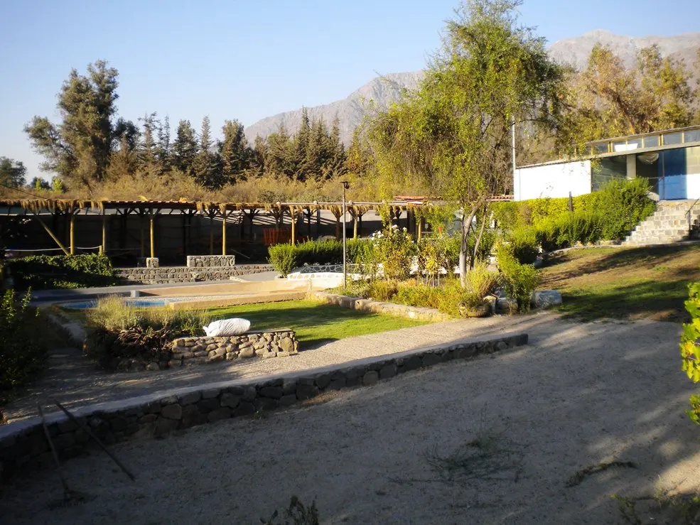 Outdoor view of a resort with pools, green grass, trees, and a mountain range in the background.
