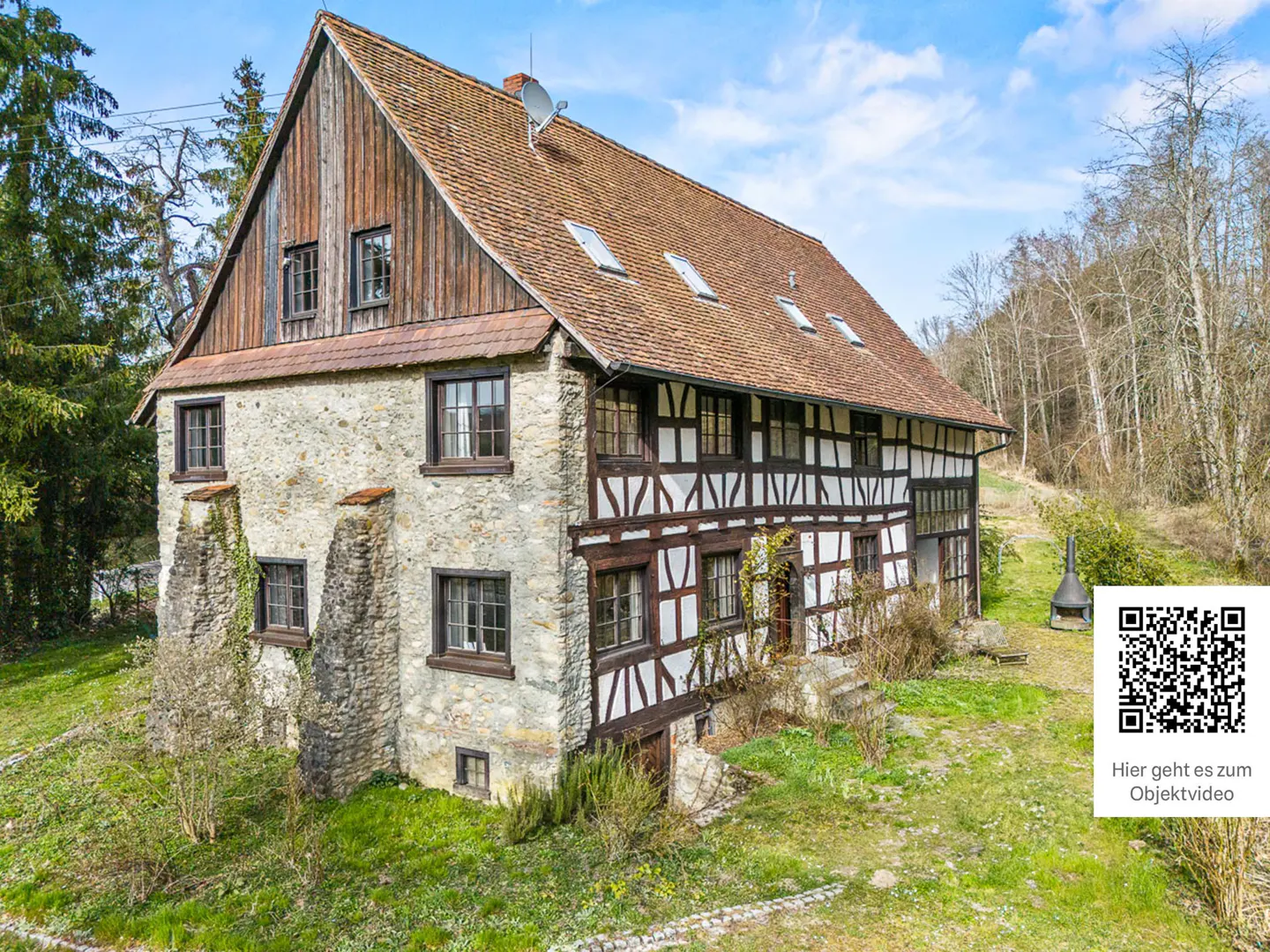 A rustic half-timbered house with stone walls, a brown tiled roof, and wooden gables set in a rural landscape.