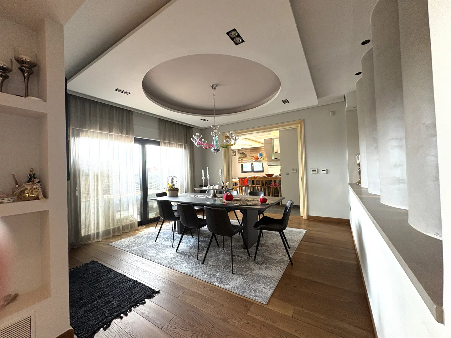 Modern dining room with a dark table, black chairs, a unique circular ceiling feature, and a view into the kitchen.